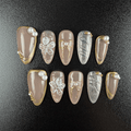 Nude almond press-on nails with gold trim and 3D flowers